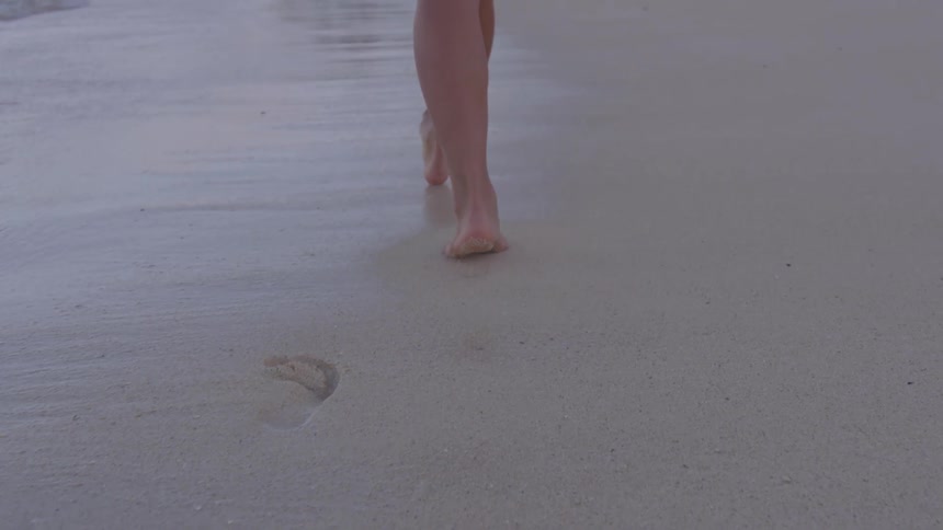 A woman walking on the beach leaving footprints in the sand