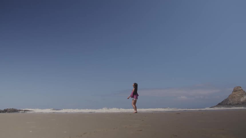 A white woman dances on a beach with a phone in her hand