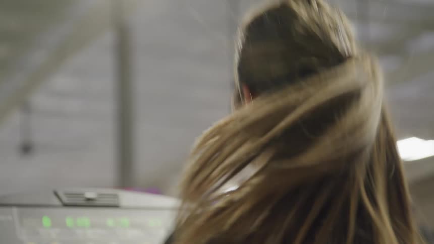A woman runs on a treadmill with her ponytail bouncing