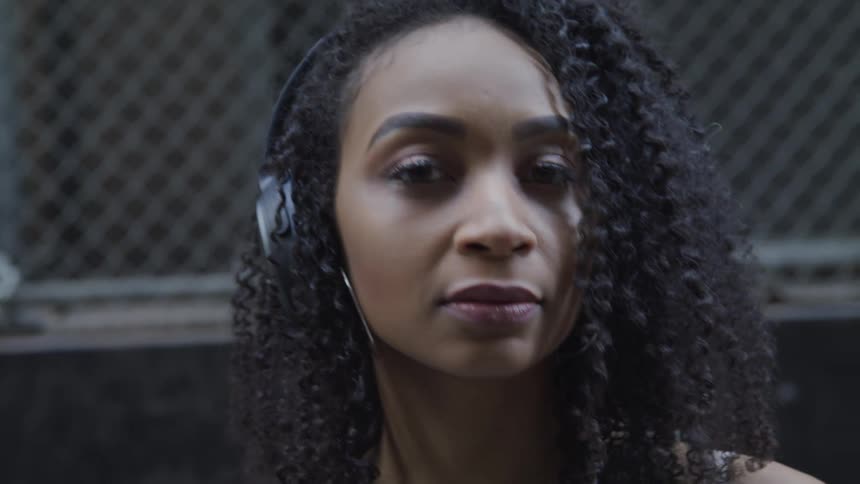 Black woman with curly hair and headphones listens to music and looks at the camera