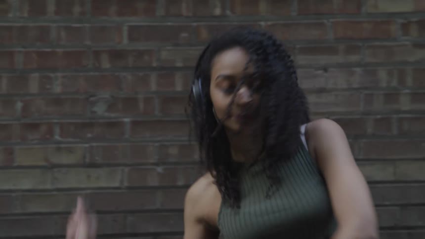 A woman with bracelets and headphones dancing with a wall in the background