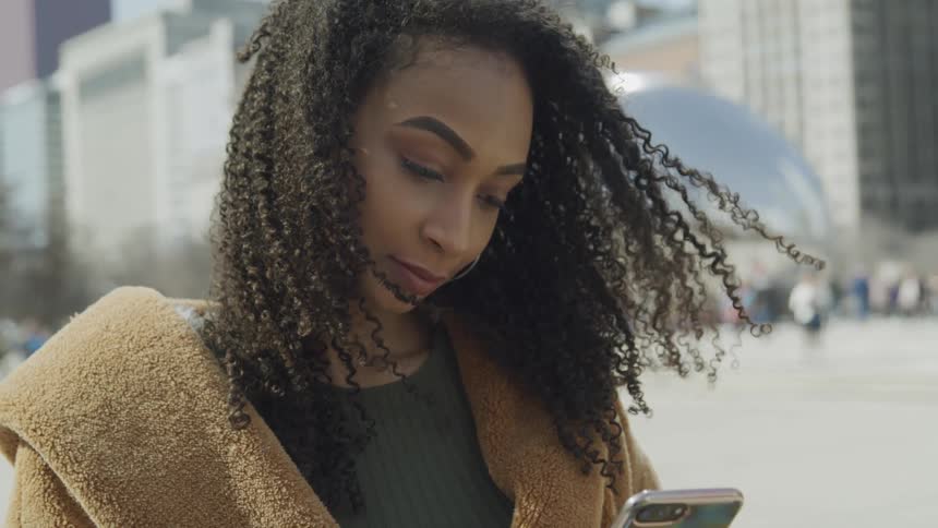 A young woman in a downtown area stands away from a crowd as she looks at her cell phone