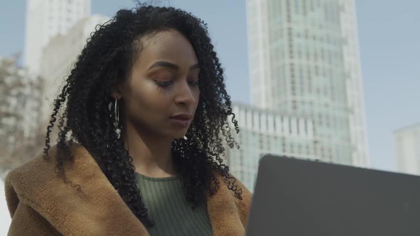 A woman is outside in the city using her laptop