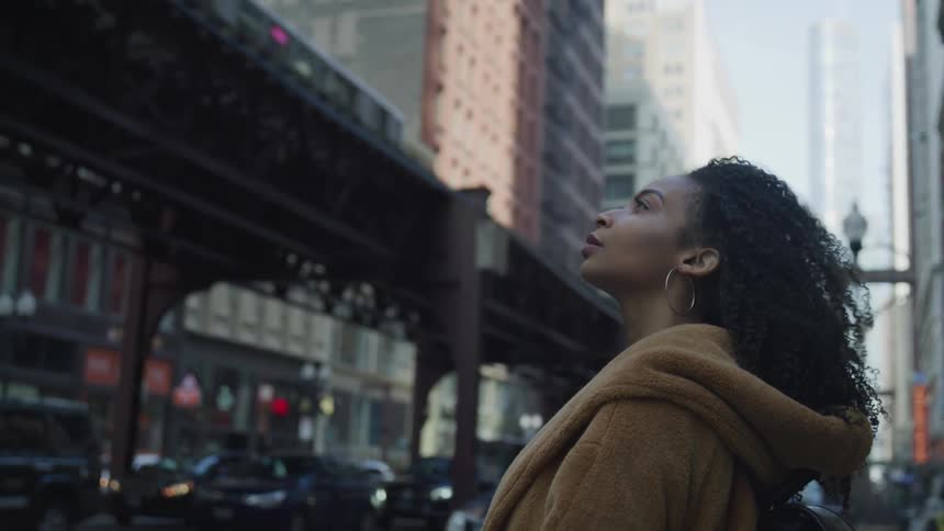 A black female standing in a downtown area observing the city