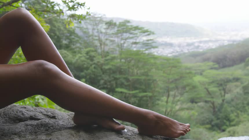 A womans legs on a wall overlooking a forest
