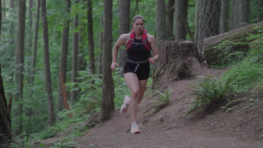 A woman is jogging through a forest