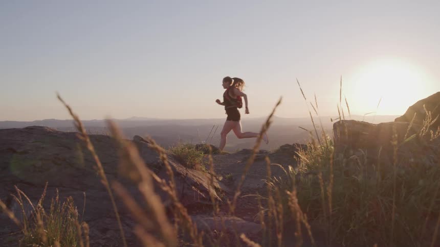 Woman runs across terrain while sun glares from horizon across foggy landscape