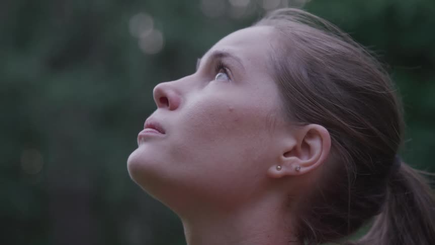 Young woman breathing and looking up while standing outdoors