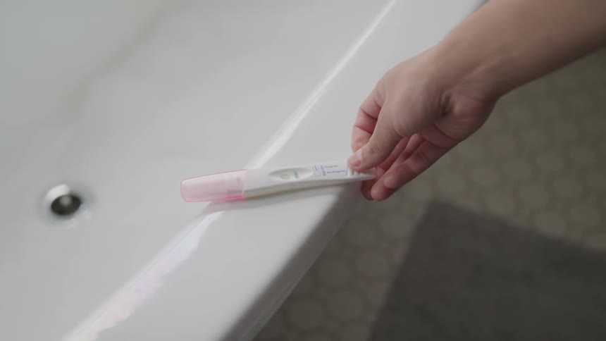 A woman places a home pregnancy test on the edge of her bathtub