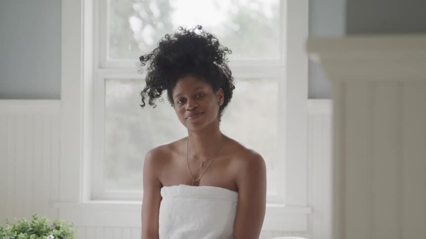 A young woman wearing a towel turns her head to smile into the camera