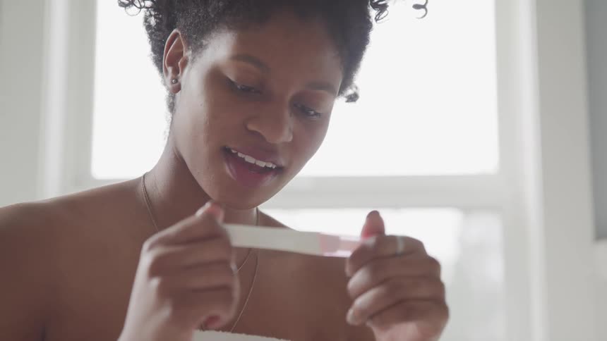 A woman sits in her bathroom with her jaw dropped as she reads the results of a pregnancy test