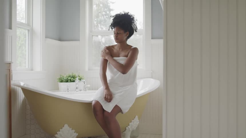 Woman wearing towel sits on edge of freestanding bathtub