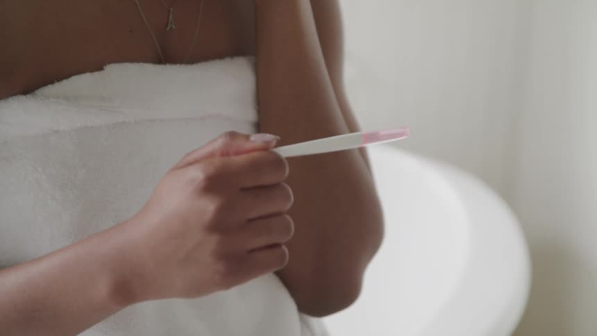 A woman in the room wrapped in a white towel looking at a pregnancy test in her hand