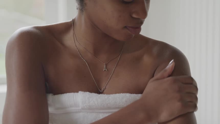 Young woman wearing a towel rubs her shoulders in the bathroom at home
