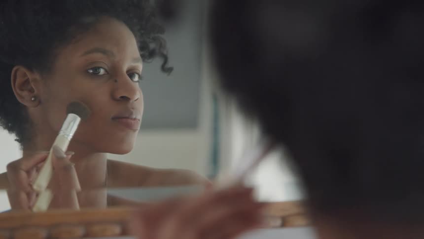 A woman is putting on makeup while looking in a mirror