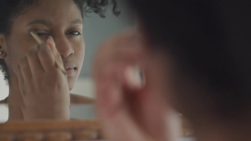 A woman is putting on makeup while looking in the mirror