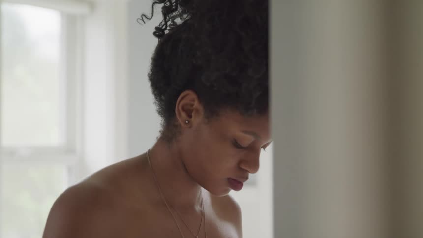 A woman stands topless in her bathroom and looks down