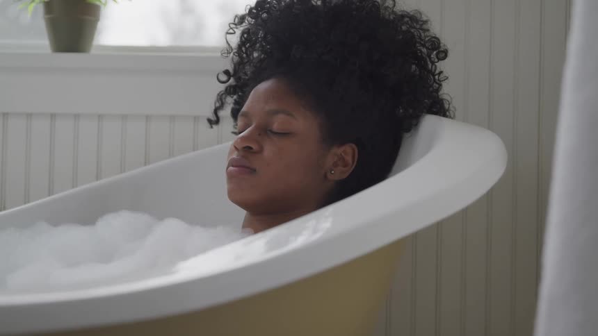 A young black woman relaxing with her eyes closed in a soapy bathtub