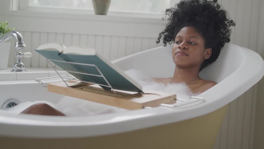 Young woman reads a book while taking a bubble bath in a bathtub at home