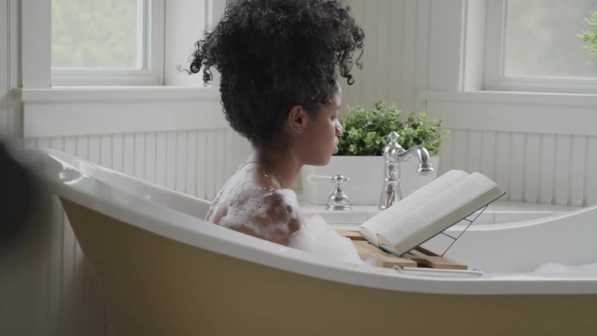 A woman reads a book while taking a bubble bath at home