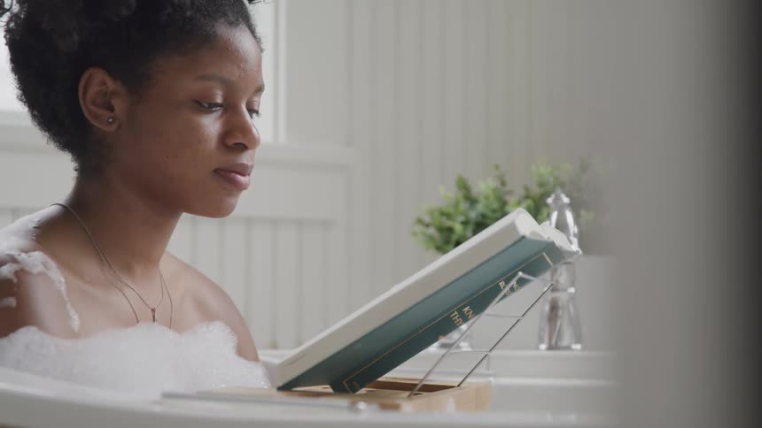 Reading a book on a display stand while taking a bubble bath
