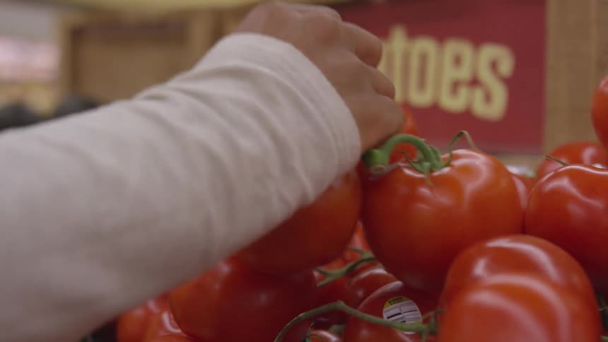 A person grabs a group of tomatoes from a vegetable stand in a grocery store
