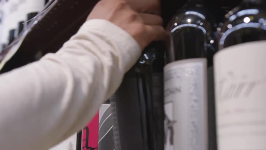 A man takes abottle of wine off a shelf in a store