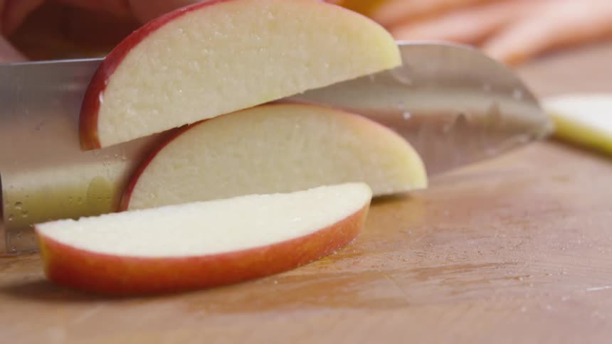 A person slicing an apple on a wood cutting board