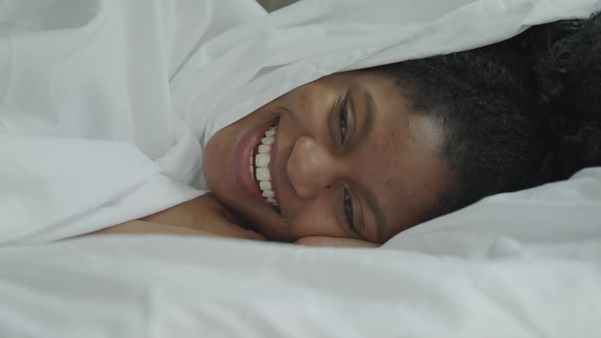 A woman laying down and smiling on a bed covered with a sheet