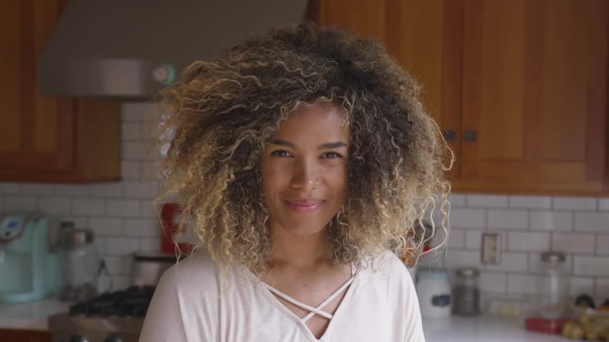Young woman with curly hair smiling in kitchen