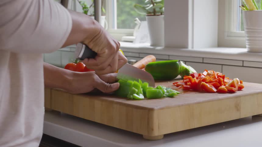 Person chopping peppers on cutting board in kitchen