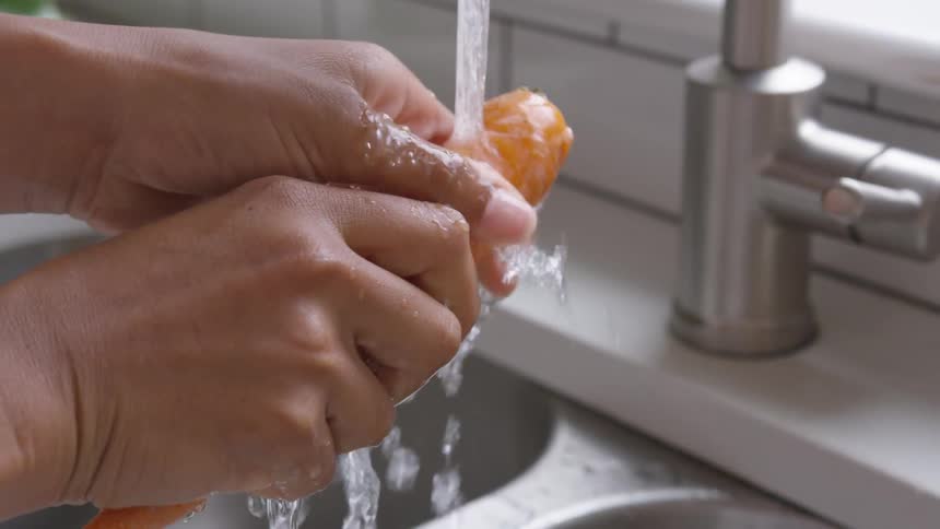 Womans hands wash a carrot under the tap in the kitchen