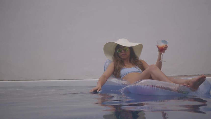 A young woman floating a pool while sipping on a cocktail