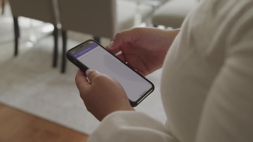 Woman uses mobile phone while standing in room with wooden floor