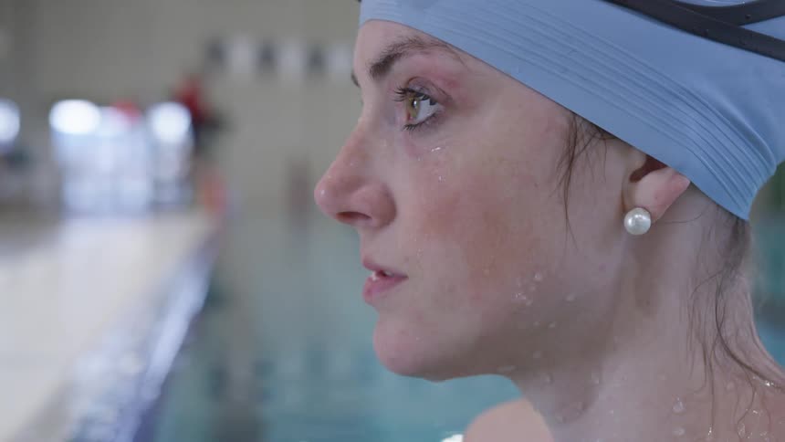 A female swimmer stands next to a pool and looks up