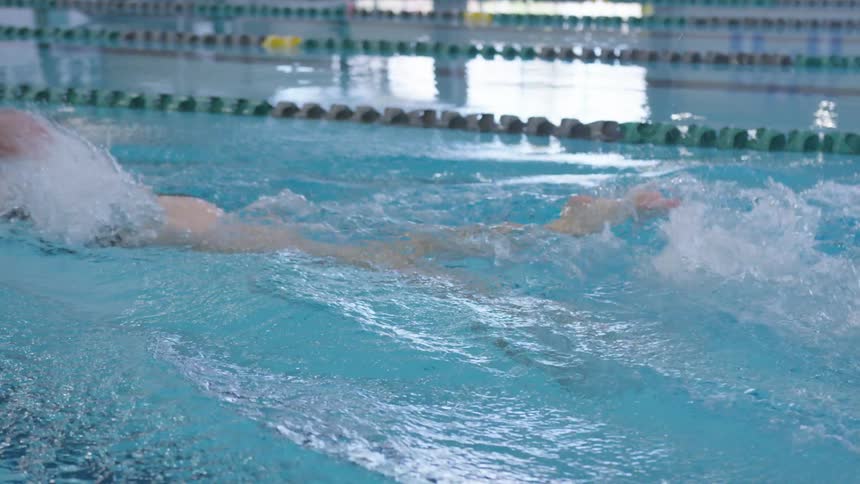 A woman in a black bathing suit swims down a lane in an indoor pool