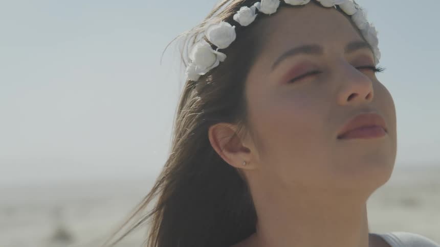A teenage girl wearing a headband of flowers stands outside with her eyes closed