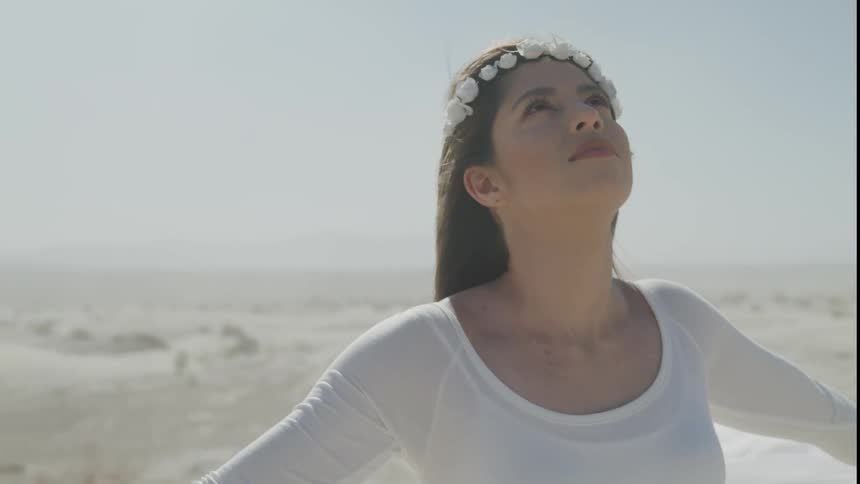 A woman with a white dress and a tiara standing on a beach with the sky in the background