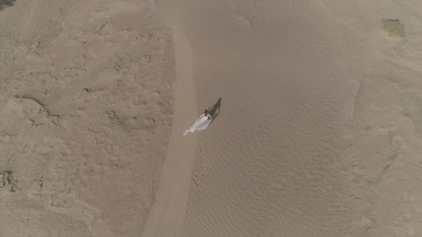 A woman in a dress walks across a sandy desert