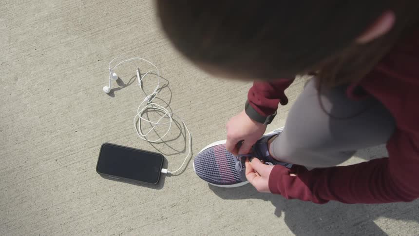 Woman lays mobile phone on ground while tying her sneaker