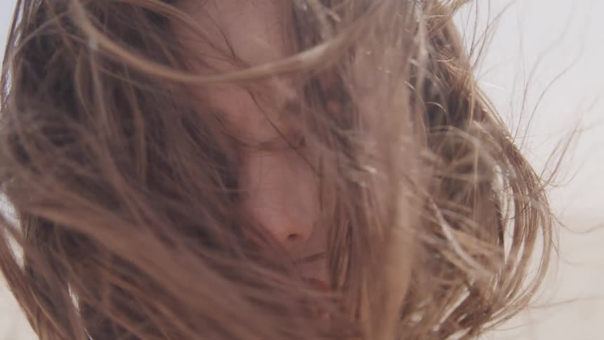 The wind blows hair across and around a womans face covering and revealing her eyes and mouth