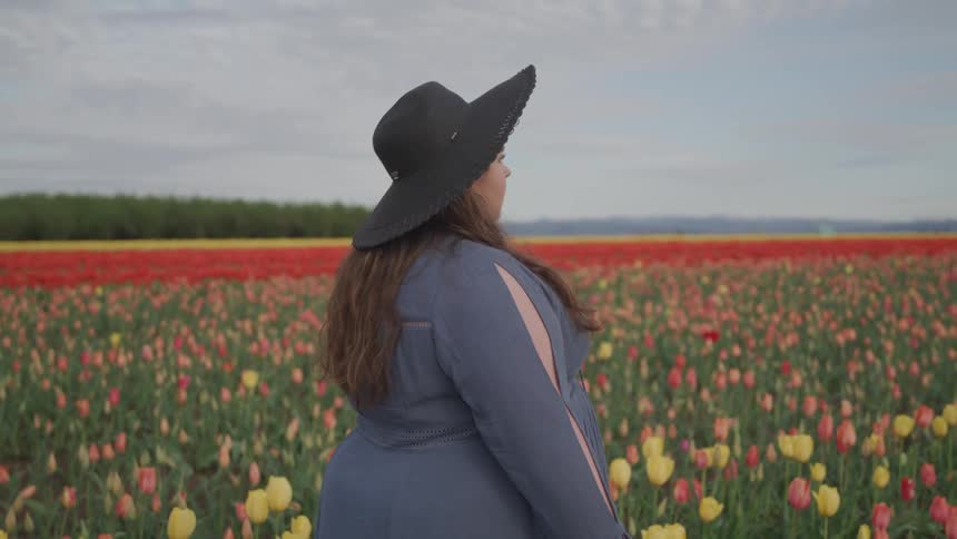 A woman in a black sunhat walks through a vast field of flowers during the day