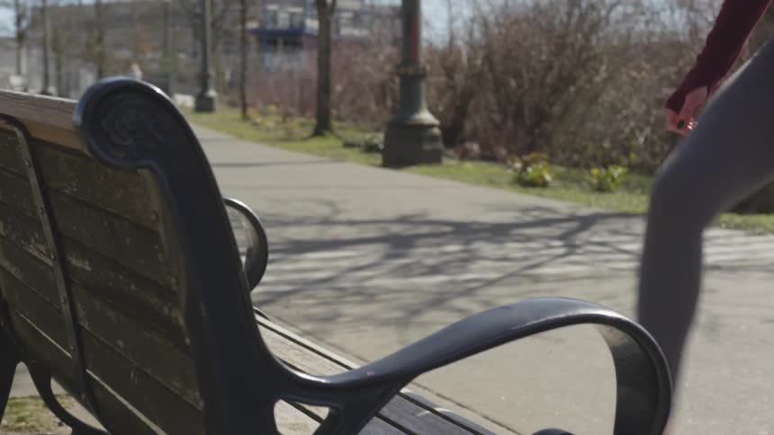 A woman stretches on a park bench as a cyclist passes by