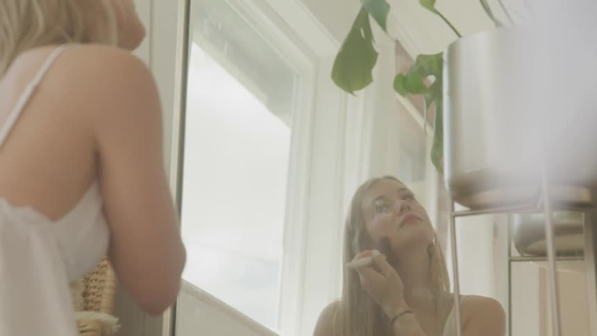A woman is putting on makeup while looking into a mirror