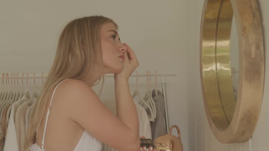 A woman putting on makeup in a mirror
