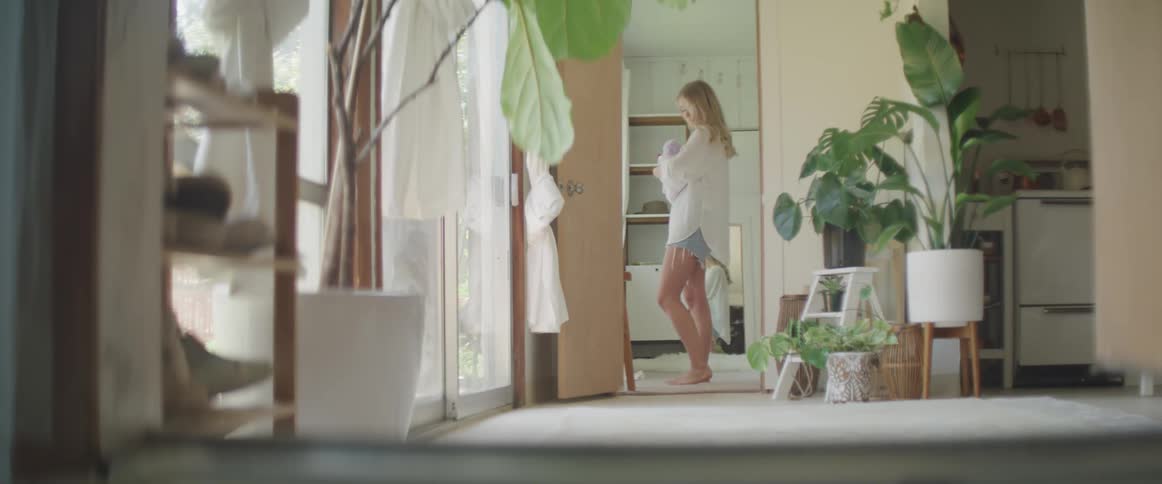 A barefoot woman stands in a sun lit house as she gently rocks a baby in her arms