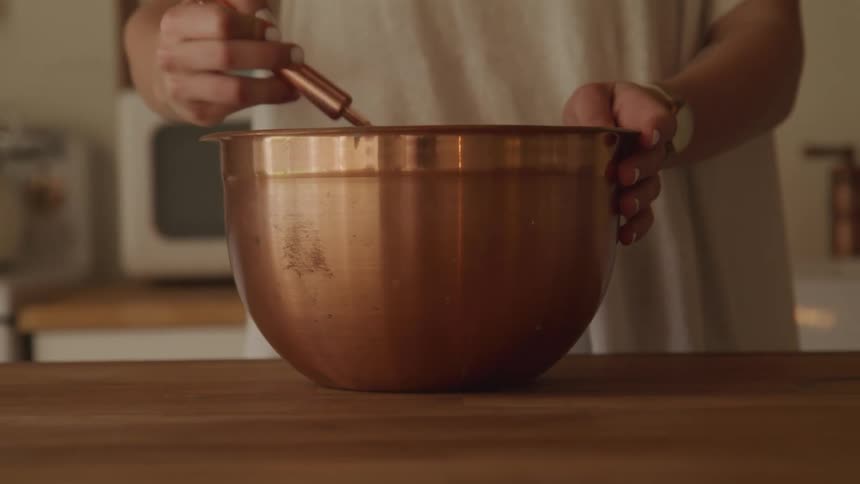 Woman mixing ingredients in copper mixing bowl with whisk