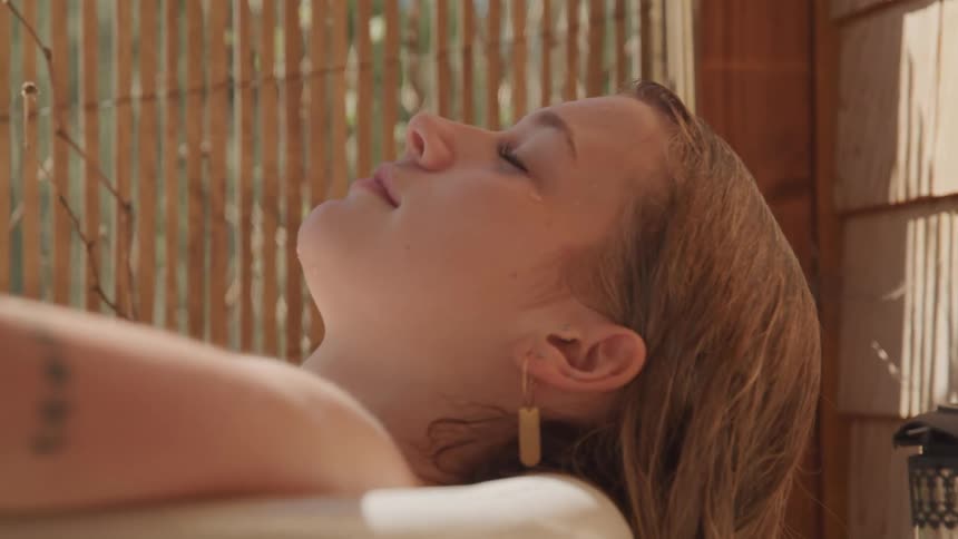 A woman rests with her eyes closed in a bathroom in a room with wooden walls
