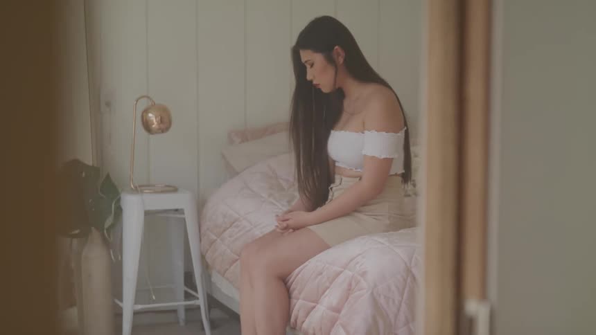 A woman in a sad mood sits on the side of a bed in a home