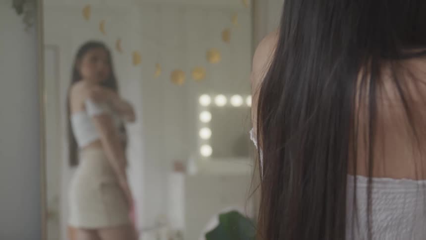 A teenage girl looks at her outfit in a mirror